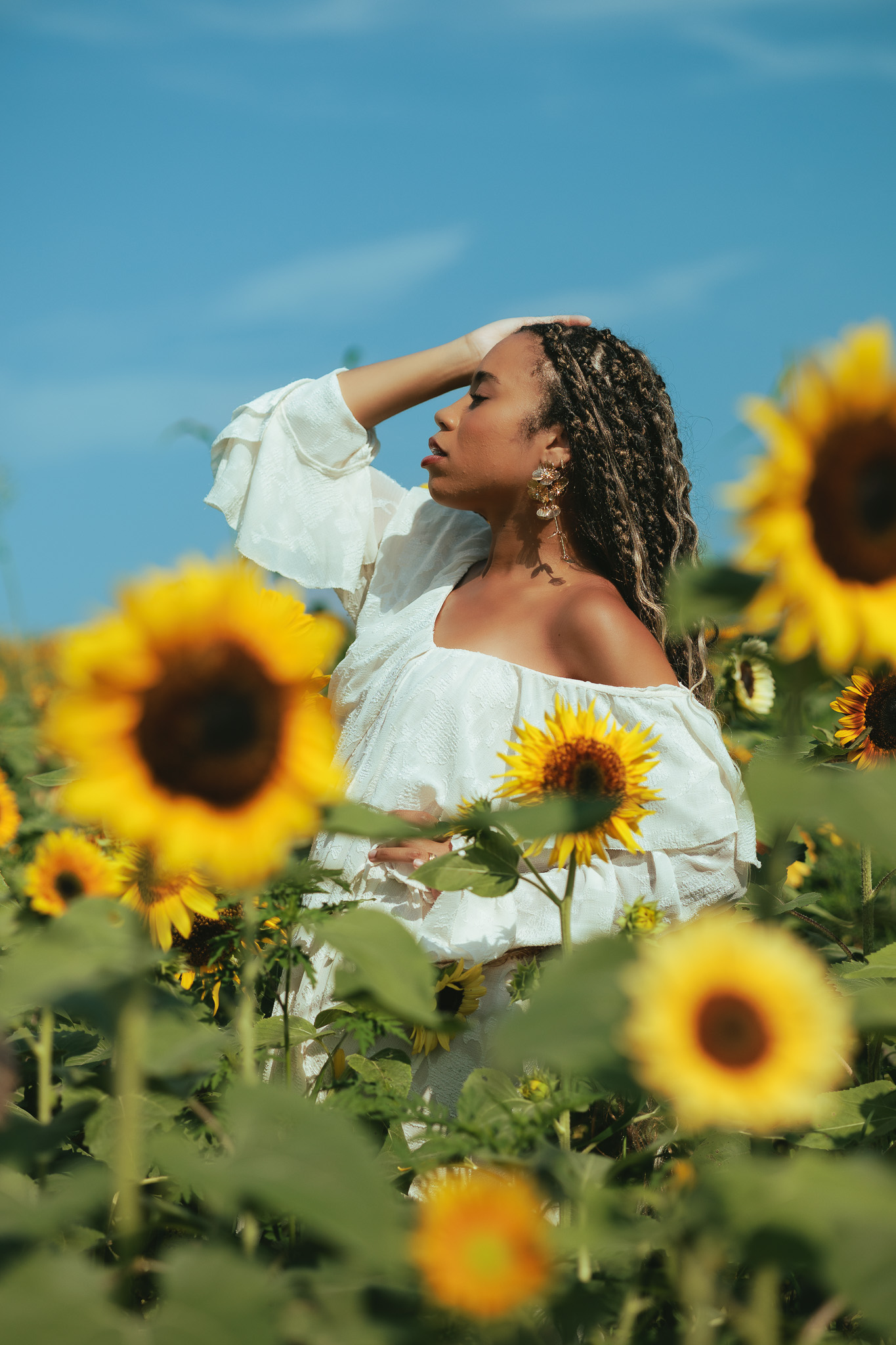 Woman holding a sunflower up to her face in the golden-hour light of the sunflower field