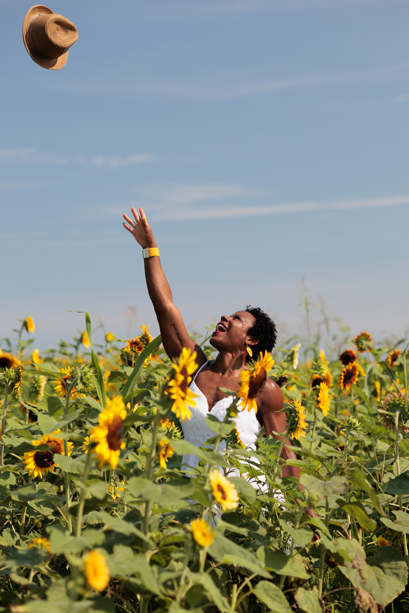 Woman joyfully tossing her hat into the sky in a sunny sunflower field